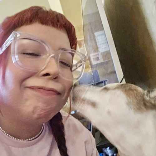 A FurBabies & Friends pet sitter receives a kiss from a white-and-tan dog while providing extra attention during a pet-sitting visit.
