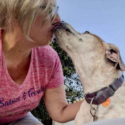 FurBabies and Friends sitter receiving a kiss from a white-and-tan dog outdoors.