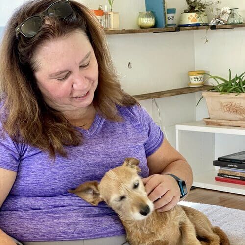 Dawn from FurBabies & Friends petting a small tan dog on a couch during a drop-in visit in Peoria AZ