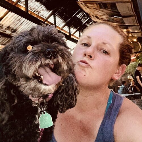 Dog trainer Kristie posing with a black Poodle mix while training at a restaurant in Phoenix AZ