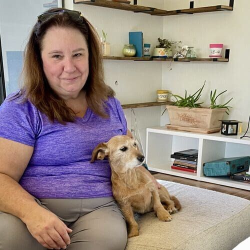 Pet sitter Dawn sitting on a couch getting snuggles from a small tan dog in Peoria AZ